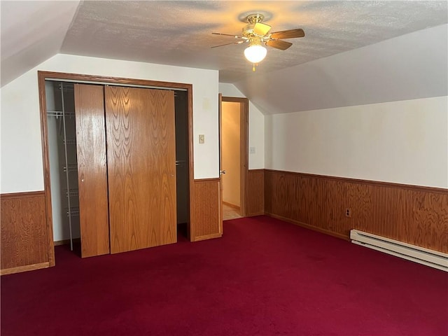 additional living space with a ceiling fan, a textured ceiling, wooden walls, and wainscoting