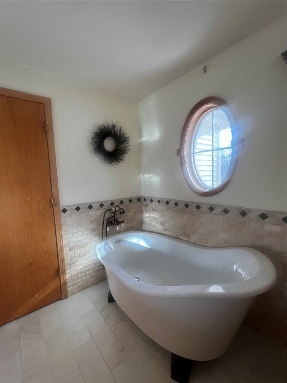 bathroom with a wainscoted wall, a freestanding tub, and tile walls