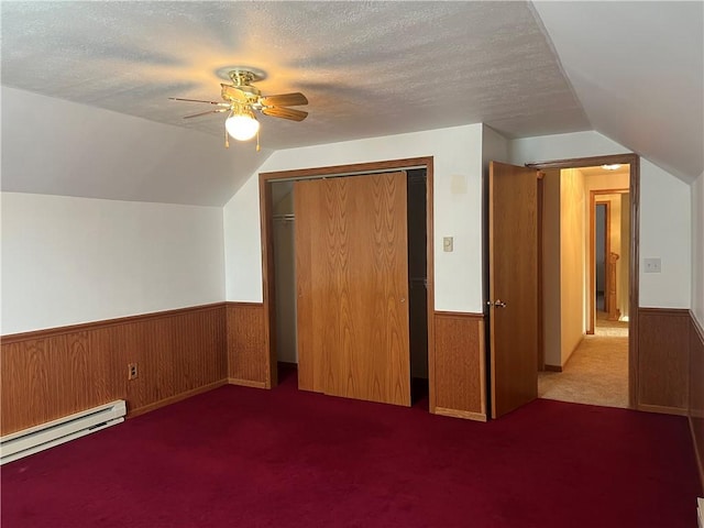 bonus room featuring ceiling fan, dark colored carpet, baseboard heating, lofted ceiling, and a textured ceiling