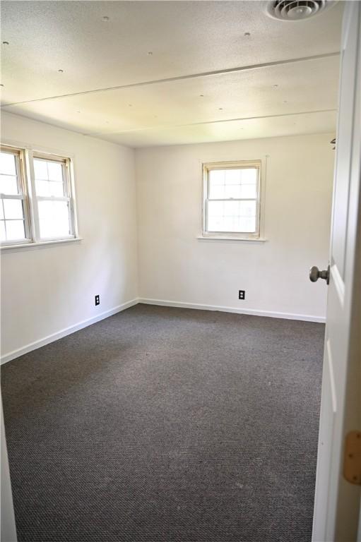 unfurnished room with a wealth of natural light and dark colored carpet