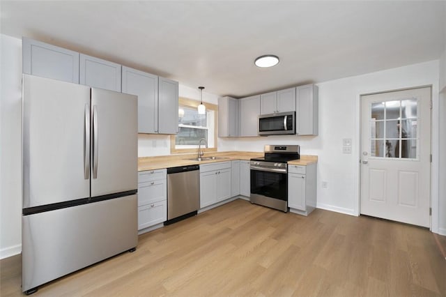 kitchen featuring decorative light fixtures, sink, appliances with stainless steel finishes, and light hardwood / wood-style flooring