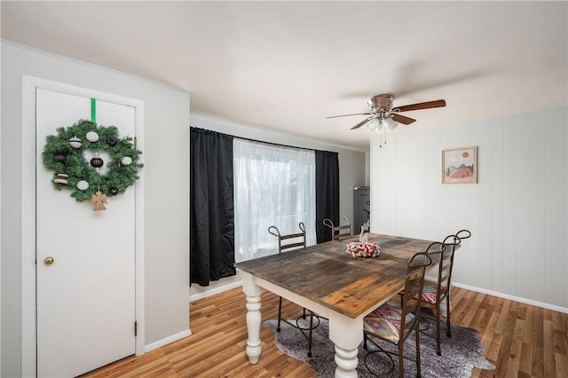 dining space with ceiling fan, wood walls, and light wood-type flooring