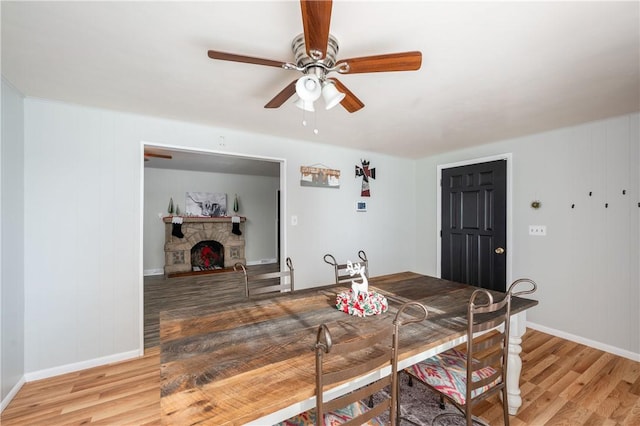 dining room featuring light wood-type flooring, a stone fireplace, and ceiling fan