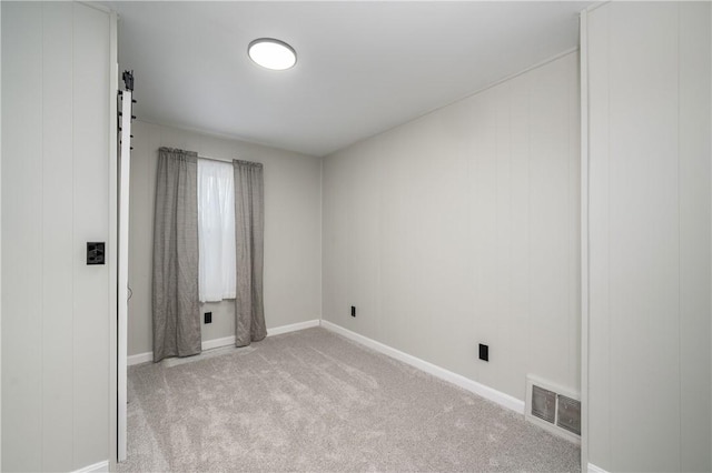 spare room featuring a barn door and light carpet