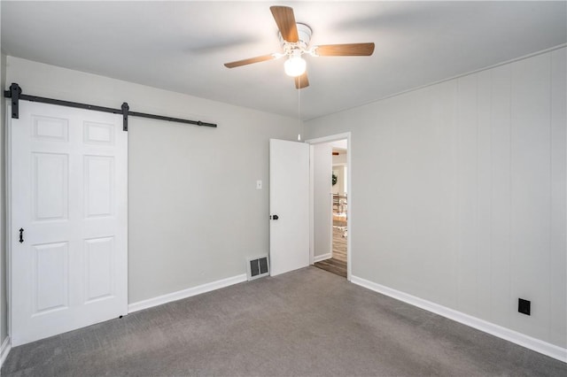 unfurnished bedroom featuring a barn door, ceiling fan, and dark carpet