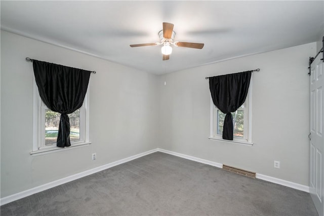 empty room featuring a barn door, ceiling fan, and dark carpet