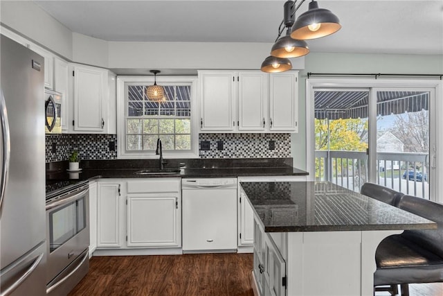 kitchen with a kitchen bar, white cabinets, stainless steel appliances, and decorative light fixtures