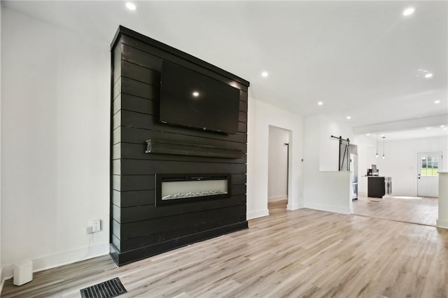 unfurnished living room with a barn door, light hardwood / wood-style flooring, and a fireplace