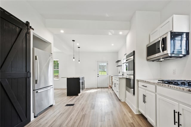 kitchen with pendant lighting, white cabinets, a barn door, light wood-type flooring, and appliances with stainless steel finishes