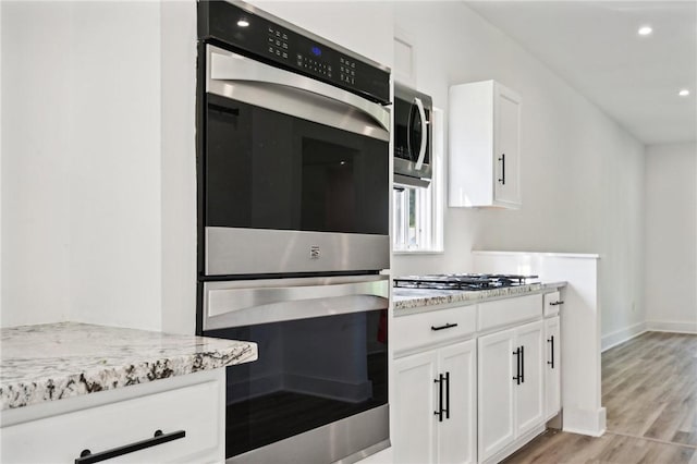 kitchen with light stone counters, light hardwood / wood-style flooring, white cabinets, and appliances with stainless steel finishes