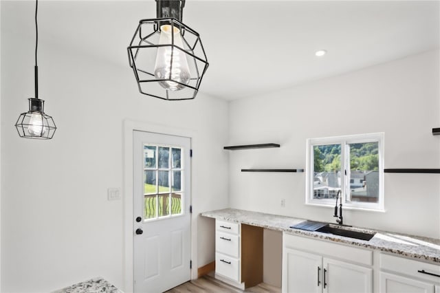 kitchen with light stone counters, sink, pendant lighting, white cabinets, and light hardwood / wood-style floors