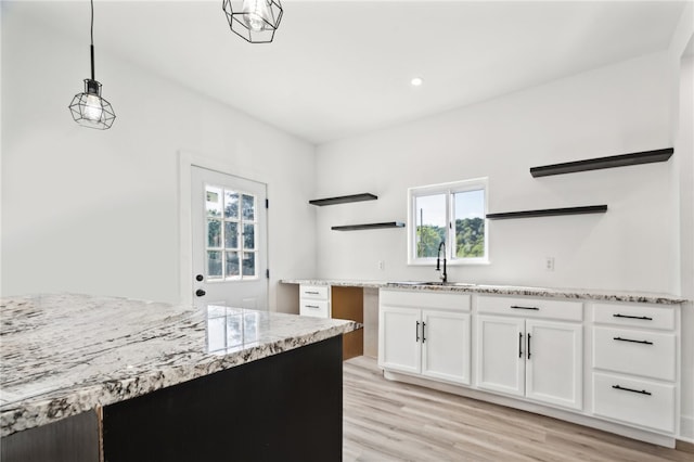 kitchen with white cabinets, pendant lighting, light stone counters, and light wood-type flooring