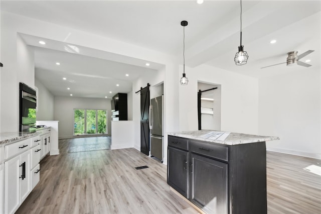 kitchen with pendant lighting, white cabinets, stainless steel fridge, a barn door, and light wood-type flooring