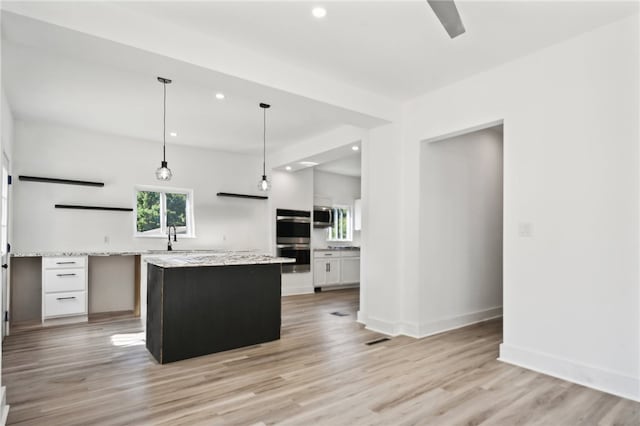 kitchen with light stone countertops, white cabinetry, a kitchen island, and hanging light fixtures