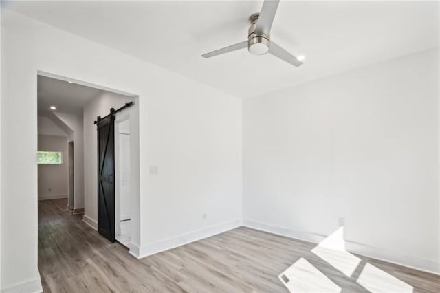 empty room with ceiling fan, a barn door, and light hardwood / wood-style flooring