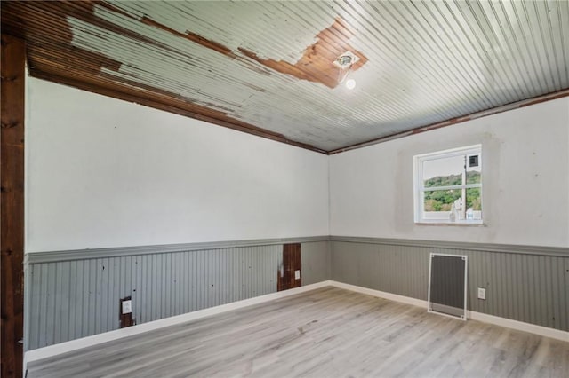 unfurnished room with wood-type flooring, ornamental molding, and wooden walls