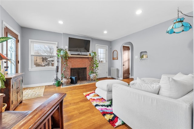 living room with hardwood / wood-style flooring, radiator heating unit, and a brick fireplace