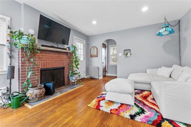 living room featuring radiator heating unit, a brick fireplace, and hardwood / wood-style floors