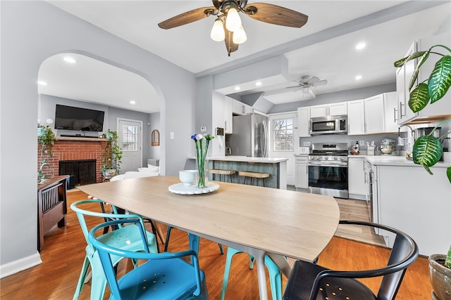 dining space with ceiling fan, light hardwood / wood-style floors, and a fireplace