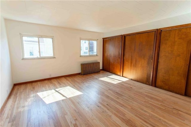 unfurnished bedroom featuring light wood-type flooring, radiator, and multiple closets