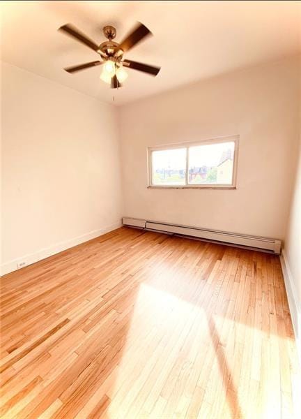 unfurnished room with light wood-type flooring, ceiling fan, and a baseboard heating unit