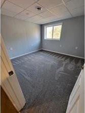 spare room featuring a paneled ceiling and dark carpet