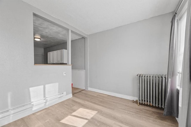 spare room with radiator heating unit, a textured ceiling, and light hardwood / wood-style flooring