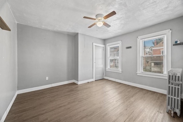 unfurnished room featuring ceiling fan, hardwood / wood-style floors, a textured ceiling, and radiator heating unit