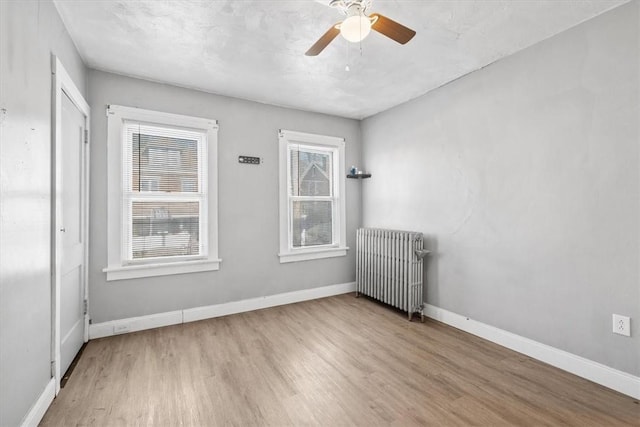 unfurnished room with light wood-type flooring, radiator, and ceiling fan