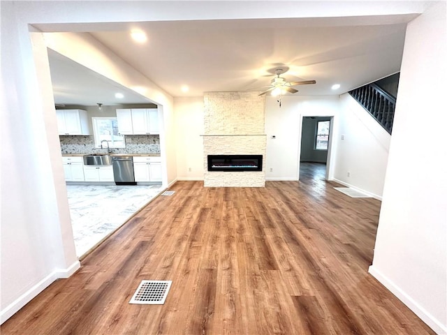 unfurnished living room featuring a stone fireplace, ceiling fan, sink, and light hardwood / wood-style floors