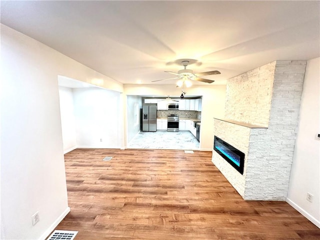 unfurnished living room featuring ceiling fan, light hardwood / wood-style floors, and a stone fireplace