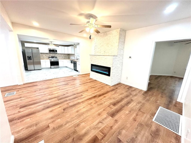 unfurnished living room featuring a stone fireplace, ceiling fan, and light hardwood / wood-style floors