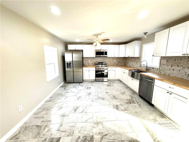 kitchen with wooden counters, tasteful backsplash, stainless steel appliances, sink, and white cabinetry