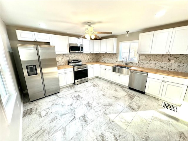 kitchen with sink, stainless steel appliances, wood counters, decorative backsplash, and white cabinets