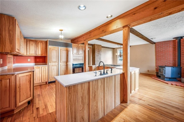 kitchen with sink, a wood stove, light hardwood / wood-style flooring, beamed ceiling, and oven