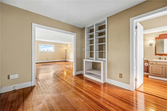 empty room featuring hardwood / wood-style floors, baseboard heating, and crown molding