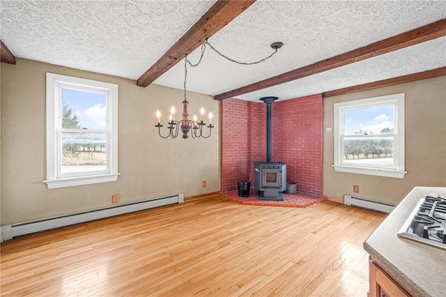 unfurnished dining area featuring beam ceiling, a wood stove, a healthy amount of sunlight, and a baseboard heating unit