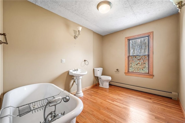 bathroom with a washtub, a baseboard radiator, hardwood / wood-style floors, a textured ceiling, and toilet