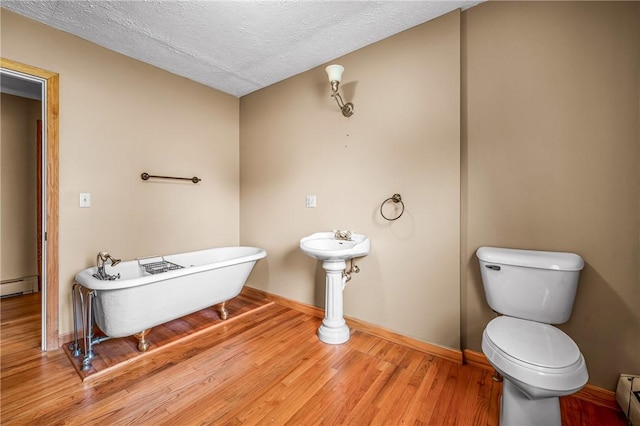 bathroom featuring a bathing tub, a baseboard radiator, a textured ceiling, toilet, and hardwood / wood-style flooring