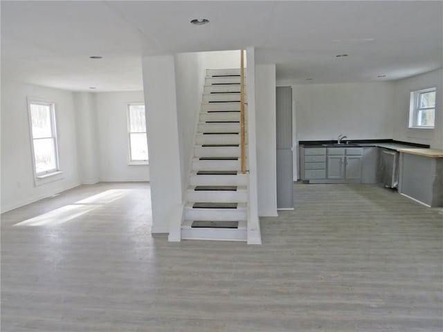 staircase featuring baseboards, wood finished floors, and a healthy amount of sunlight