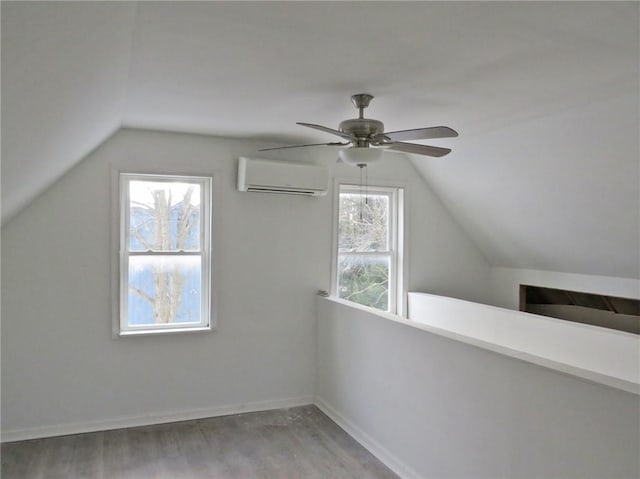 additional living space featuring baseboards, a ceiling fan, lofted ceiling, wood finished floors, and a wall mounted air conditioner