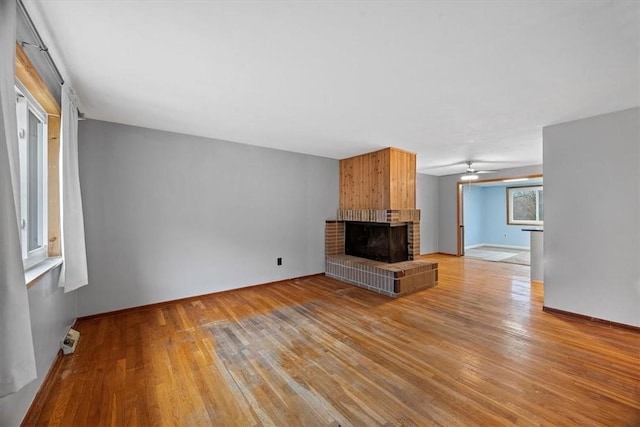 unfurnished living room with ceiling fan, light wood-type flooring, and a brick fireplace