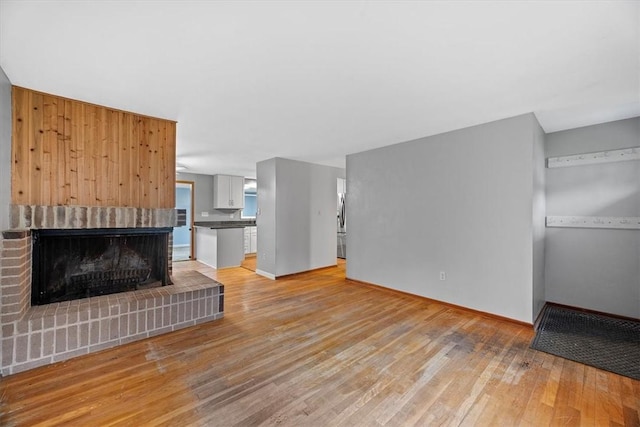 unfurnished living room featuring light hardwood / wood-style flooring and a brick fireplace