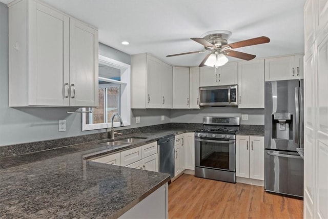 kitchen with dark stone counters, white cabinets, sink, light hardwood / wood-style flooring, and stainless steel appliances