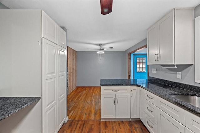 kitchen with dark stone countertops, white cabinetry, ceiling fan, and wood-type flooring