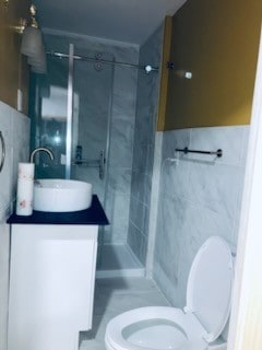 bathroom with a tile shower, vanity, tile walls, and toilet