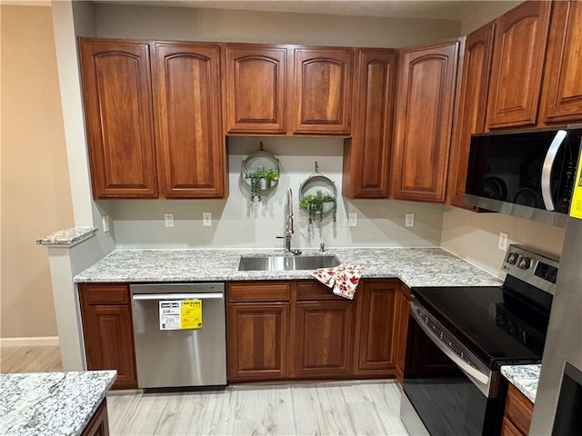 kitchen featuring appliances with stainless steel finishes, light stone counters, light hardwood / wood-style flooring, and sink