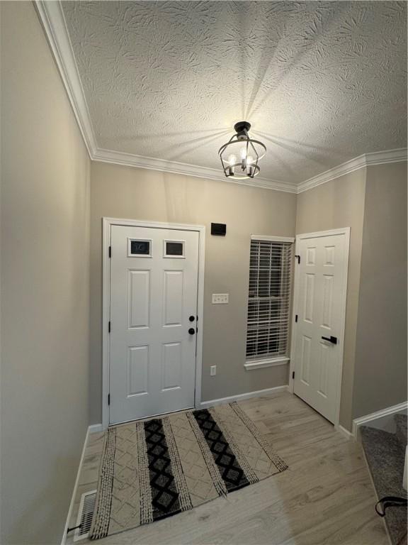 entryway with a chandelier, a textured ceiling, light hardwood / wood-style flooring, and ornamental molding