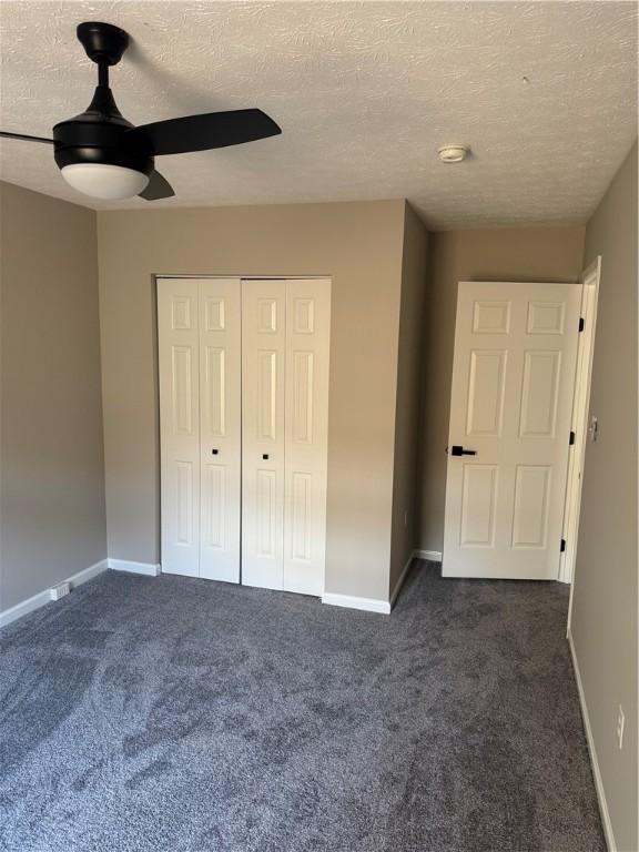 unfurnished bedroom with dark colored carpet, a textured ceiling, a closet, and ceiling fan