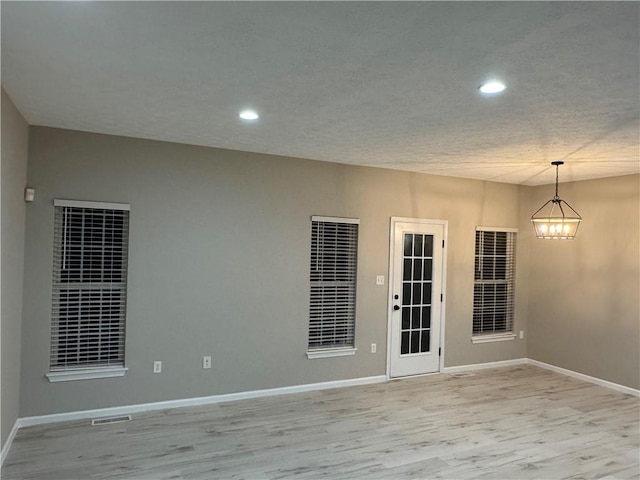 unfurnished room with an inviting chandelier and light hardwood / wood-style flooring